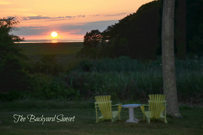 View of sunset over cape cod marsh with yellow adirondack chairs in foreground